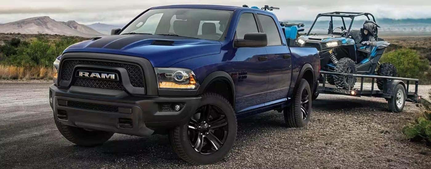 A blue 2023 used Ram 1500 Classic for sale towing an ATV.