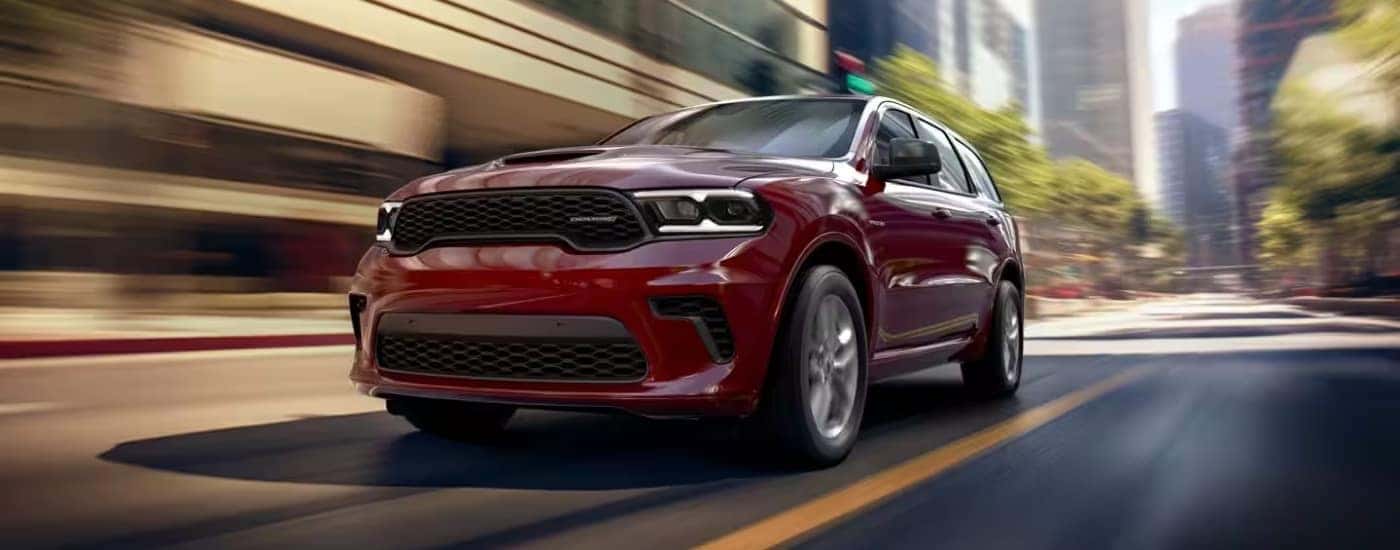 A red 2025 Dodge Durango is shown driving on a city street after visiting a Dodge dealer.