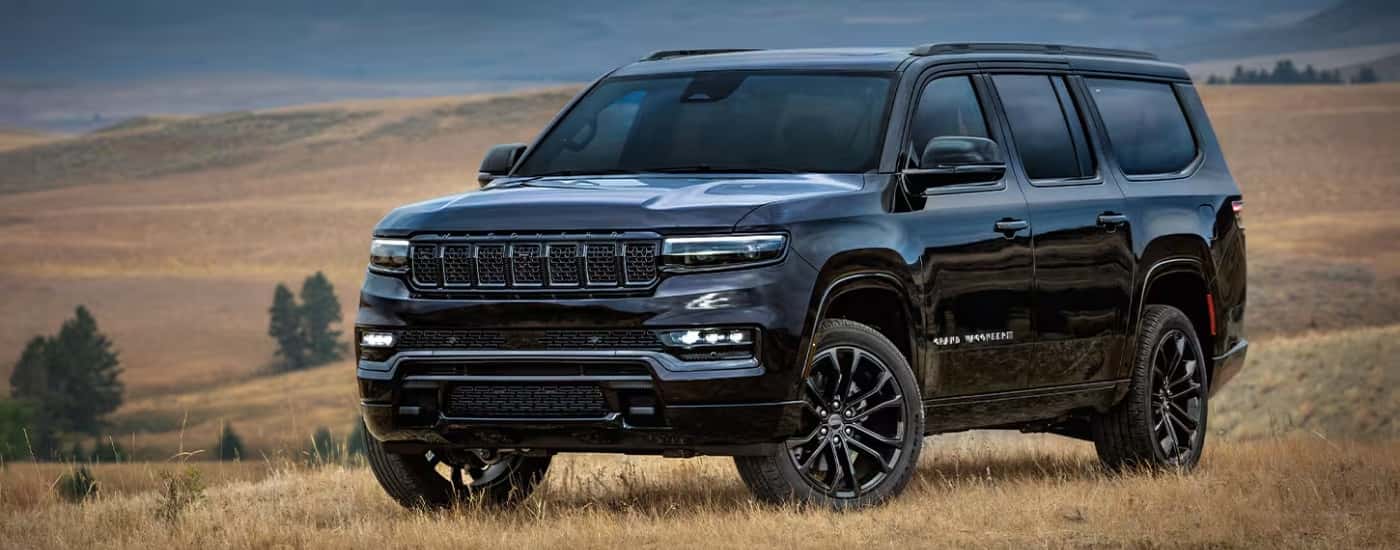 A black 2025 Jeep Grand Wagoneer parked on a dry grassy field.