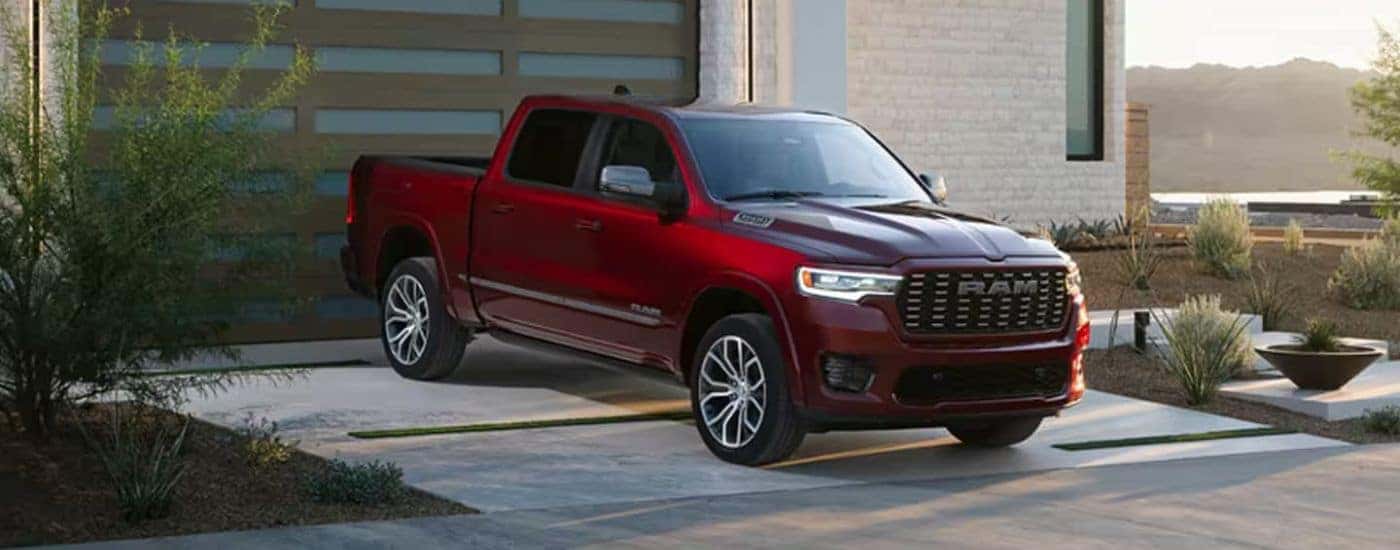 A red 2025 Ram 1500 for sale parked in front of a garage.