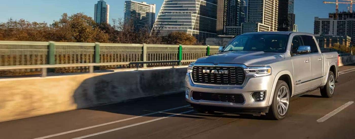A silver 2025 Ram 1500 is driving on a highway through a city after leaving a Ram dealer.