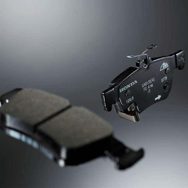3 Main Benefits of Using OEM parts for your vehicle at Washington Honda in Washington, PA | Honda Genuine Part Brake Pads Floating in Air Angled on Gray Background With One Brake Pad Blured in Foreground and one Sharp in Background