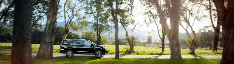 The 2022 Honda Pilot vs The 2022 Subaru Ascent at Washington Honda | Side view of a Black Honda Pilot driving on the road with alot of trees and grass around it