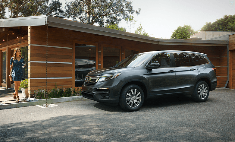 The 2022 Honda Pilot vs The 2022 Subaru Ascent at Washington Honda | Side view of dark grey Honda Pilot parked outside of house, where a women is walking up to it