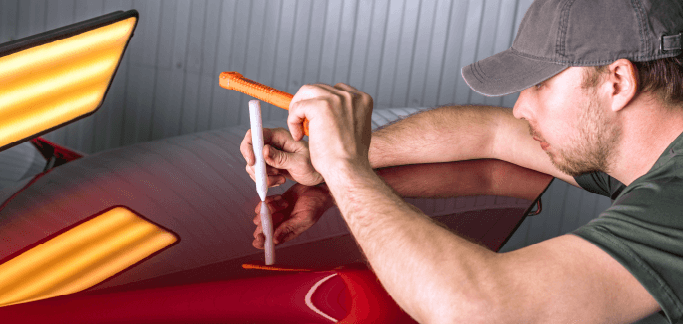 What is Paintless Dent Repair? | Washington Honda | Man using a special tool to even out red car roof while a special yellow light is on the left side
