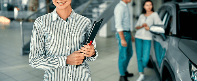 Vehicle Registration Taxes and Fees at Washington Honda in Washington, PA | Sales person in white and blue button up shirt is holding a clipboard while a couple is in the background car shopping